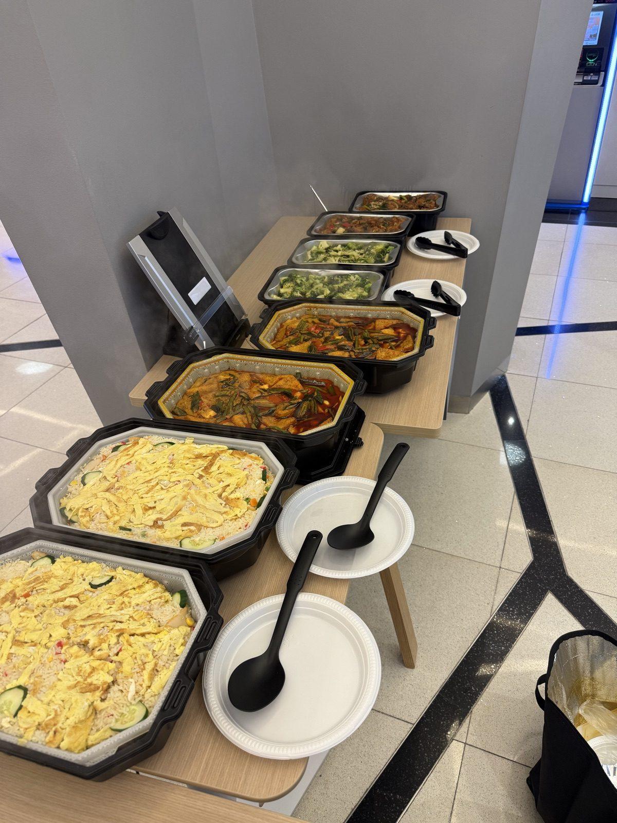 Self-heating trays of curries and noodles along a service counter with plates stacked