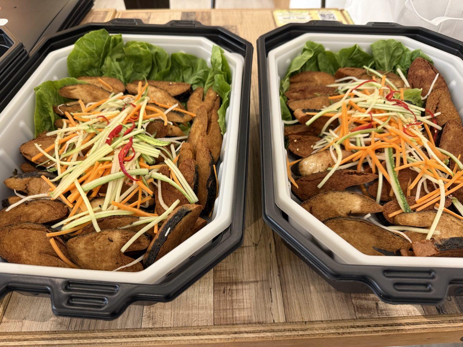 Two self-heating trays of fried fish topped with shredded green mango salad